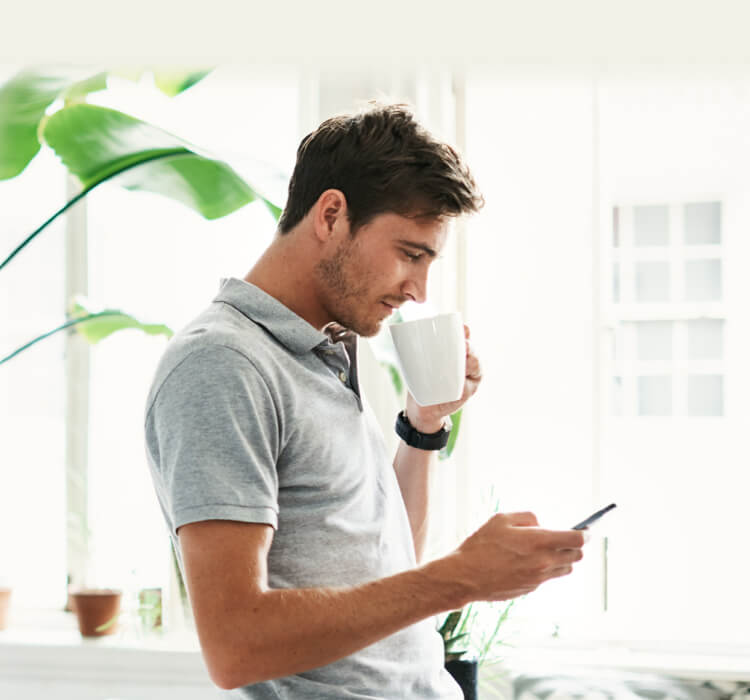 Homem bebendo café enquanto segura o telefone celular