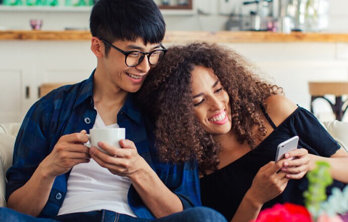 homem e mulher no sofá olhando para o celular protegido por Norton 360 for Mobile.